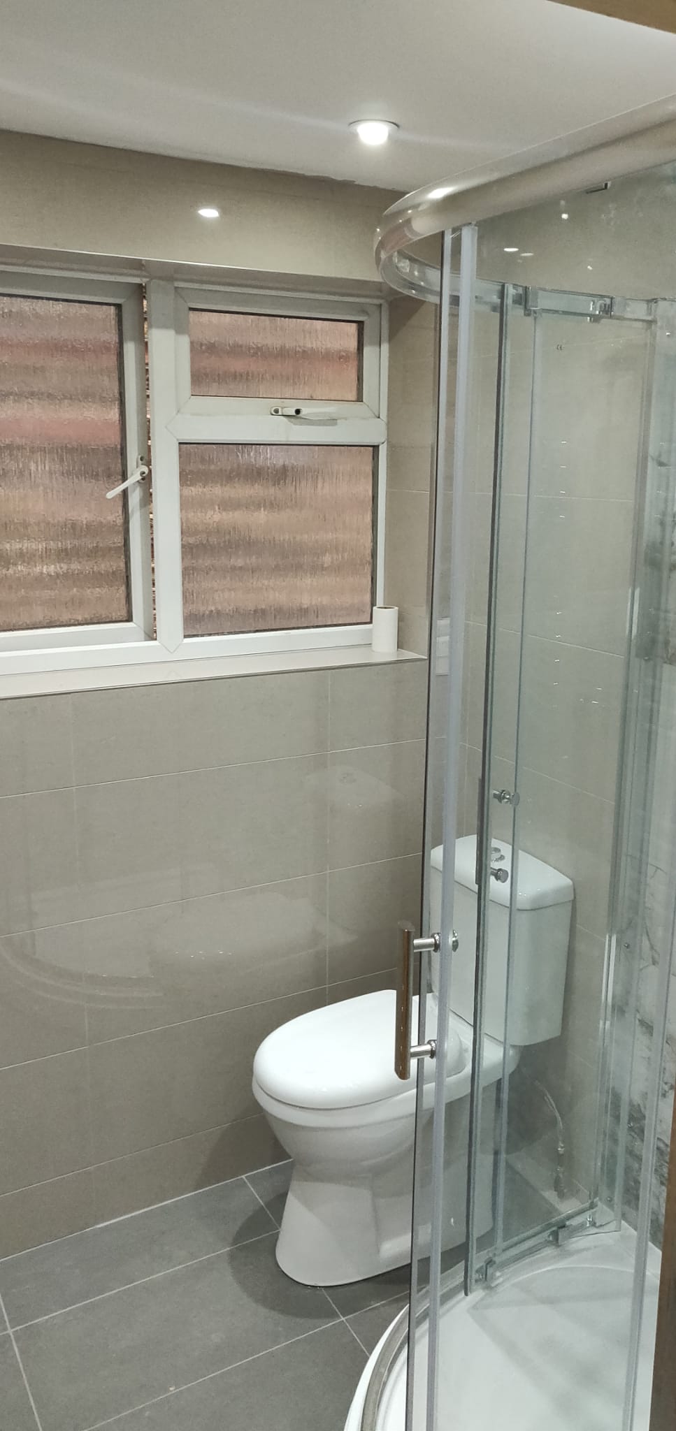 Finished compact bathroom with shower enclosure and tiled walls